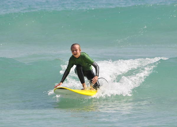 Ein lachendes Mädchen auf einem Softboard in einer kleinen grünen Welle